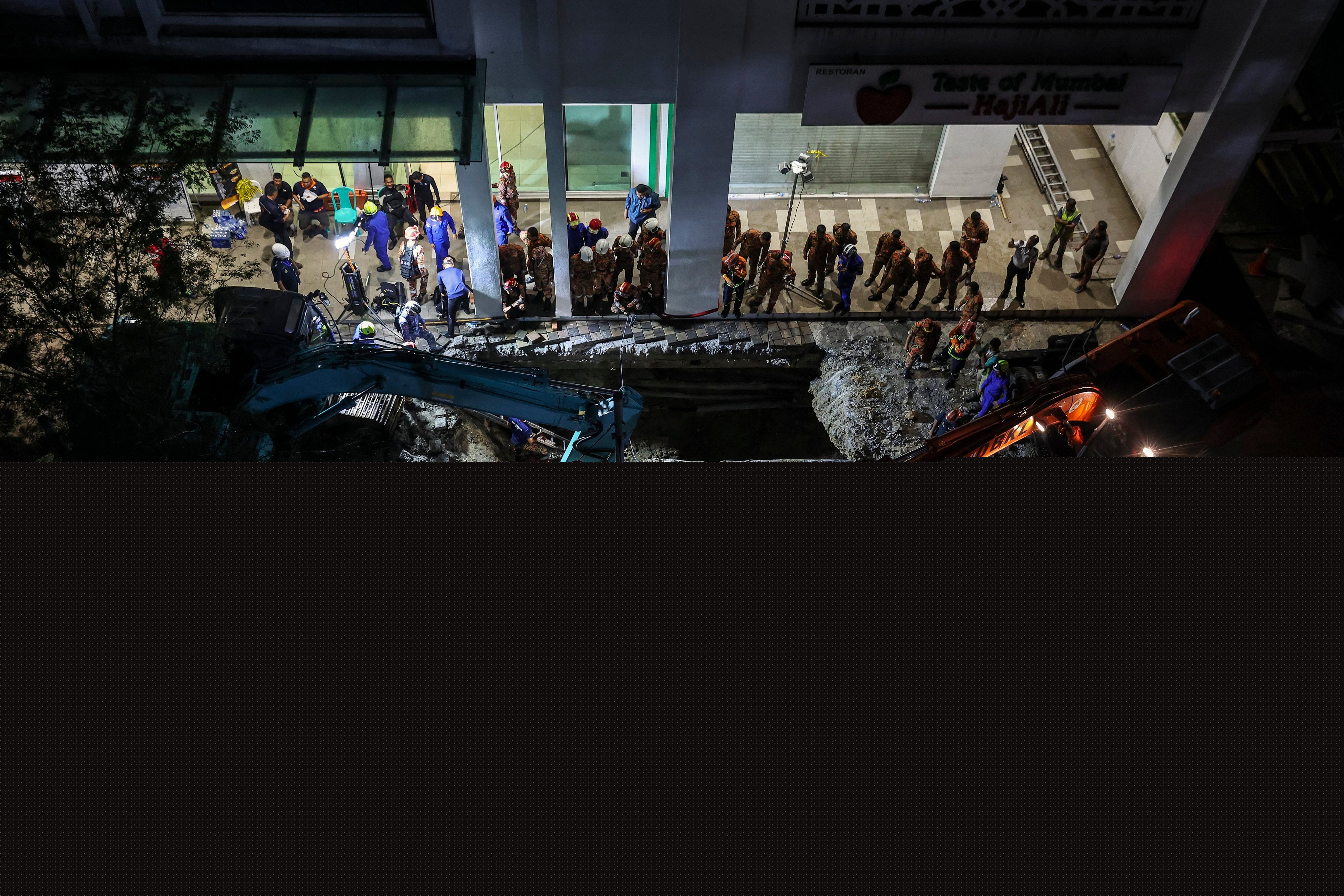 Rescuers inspect the site where a woman fell into the sinkhole in Kuala Lumpur on Friday. Photo: EPA-EFE