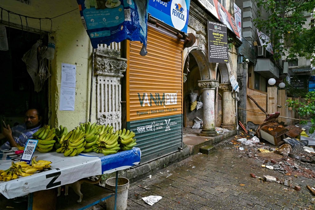 A fruit vendor waits for customers near a warning notice for evacuation stuck outside a building, demarcated as highly dilapidated by the civic authorities, in Mumbai. Photo: AFP